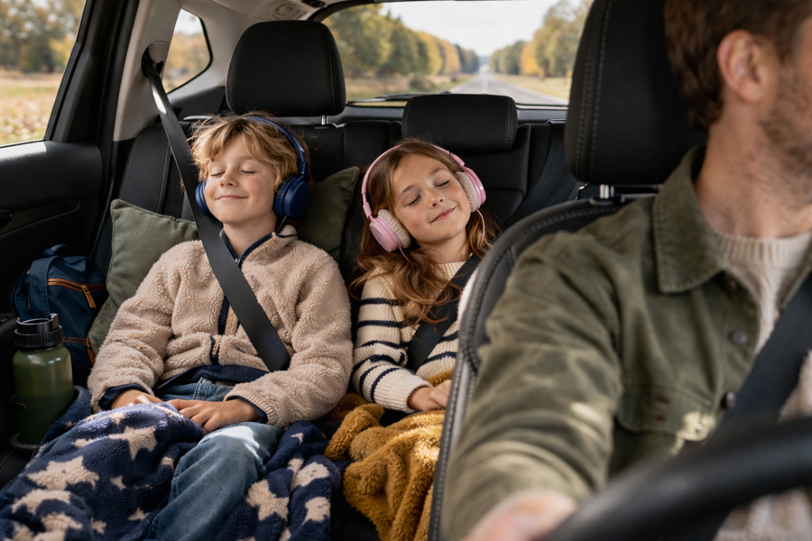 Två barn med hörlurar sitter nöjda i baksätet under en bilresa och lyssnar på ljudböcker